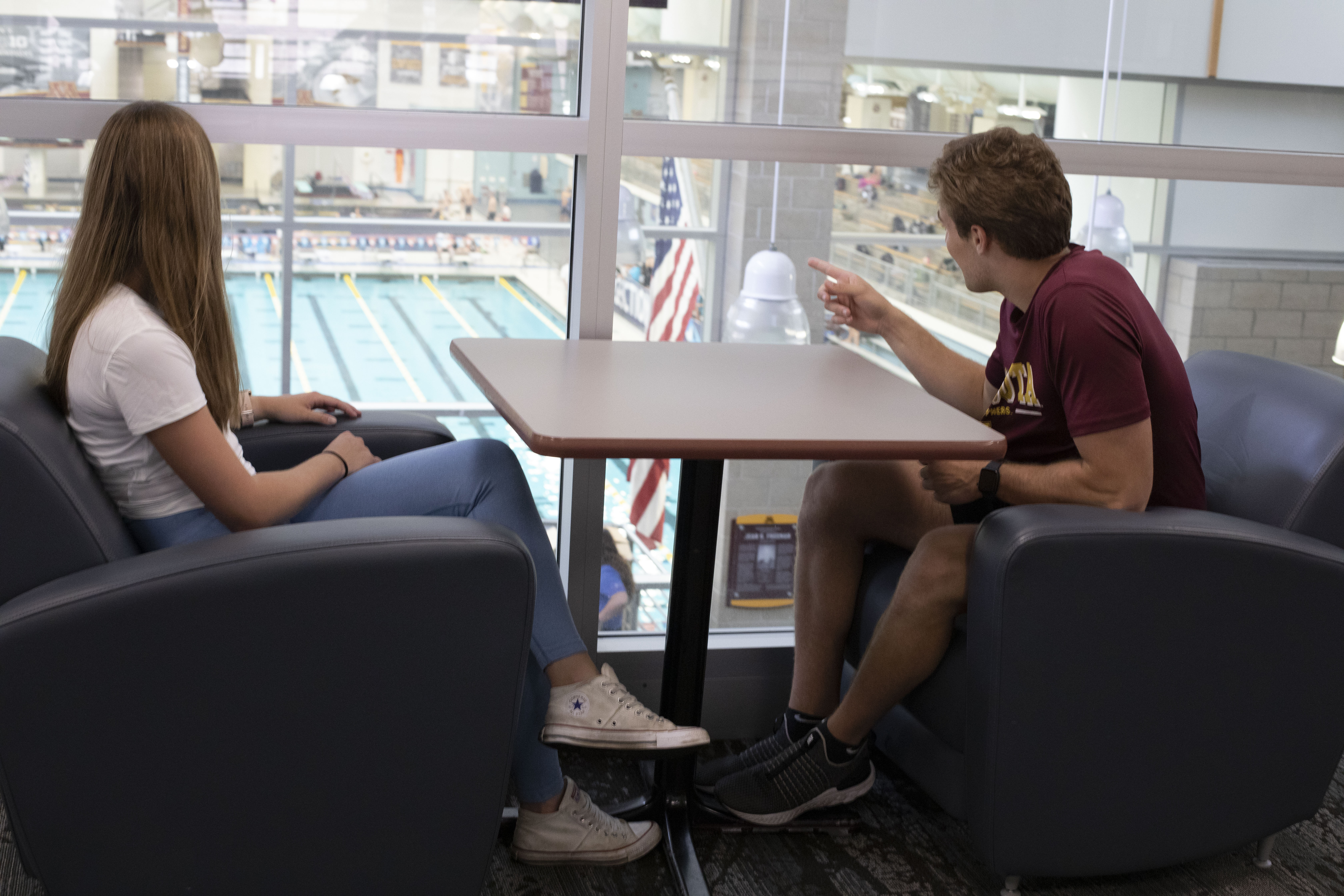 students sitting in chairs pointing out window at pool